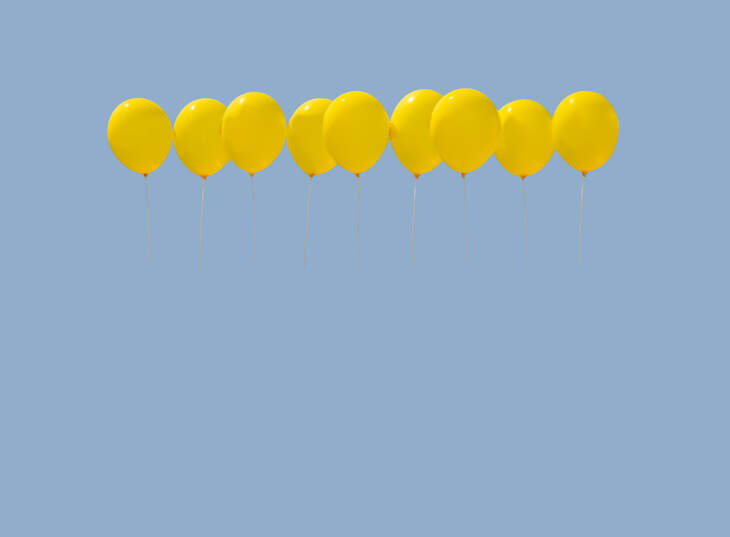 Nine yellow balloons soaring against light blue sky with copy space.